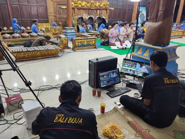 Kru berjaket Bali Buja duduk di meja kontrol produksi menghadap monitor saat pentas gamelan berlangsung.