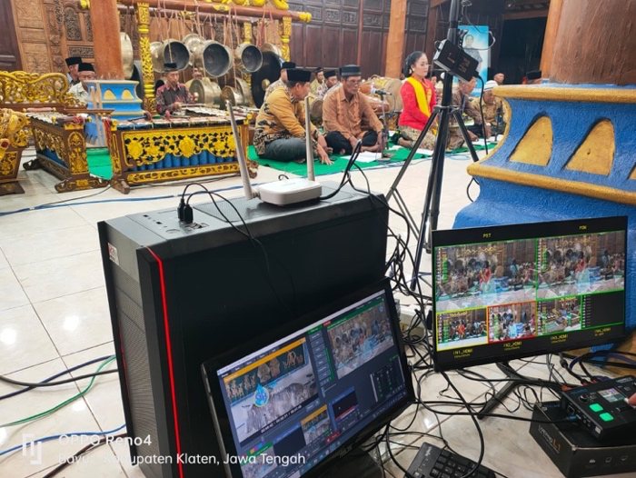 Meja kontrol siaran di pendopo: monitor multiview, mixer audio, dan kabel di depan panggung pengrawit.